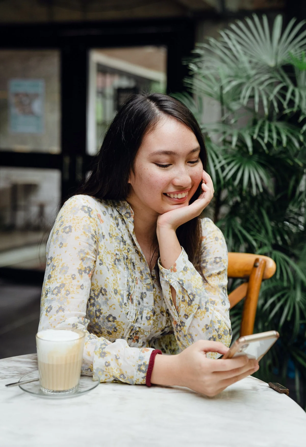Mulher usando o celular enquanto toma um café